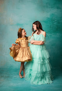 "Mint green tiered gown with delicate off-shoulder straps and floral headpiece."
