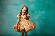 "Shimmering gold dress with a structured skirt and puff sleeves, worn by a young girl."
