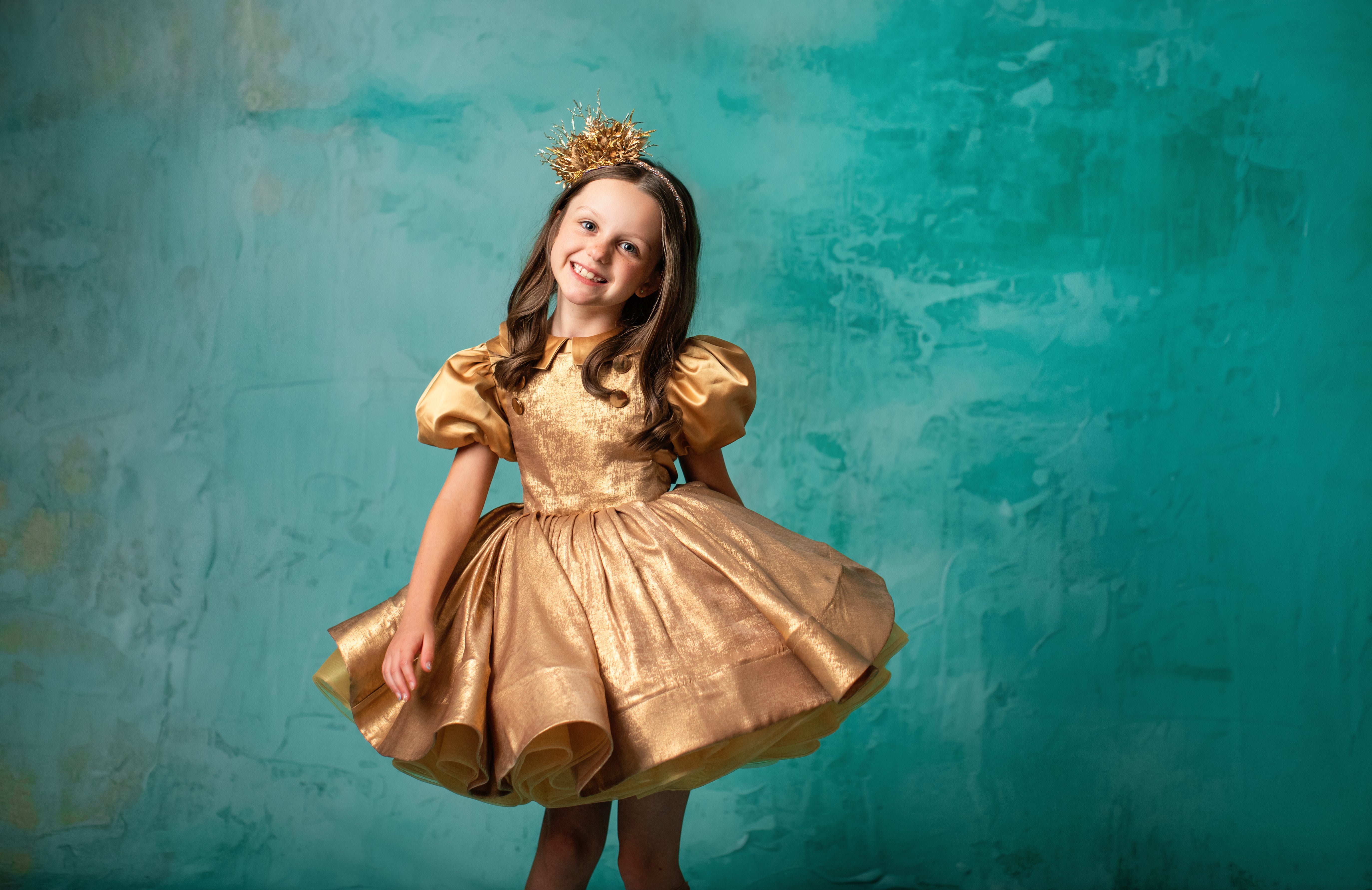 "Shimmering gold dress with a structured skirt and puff sleeves, worn by a young girl."
