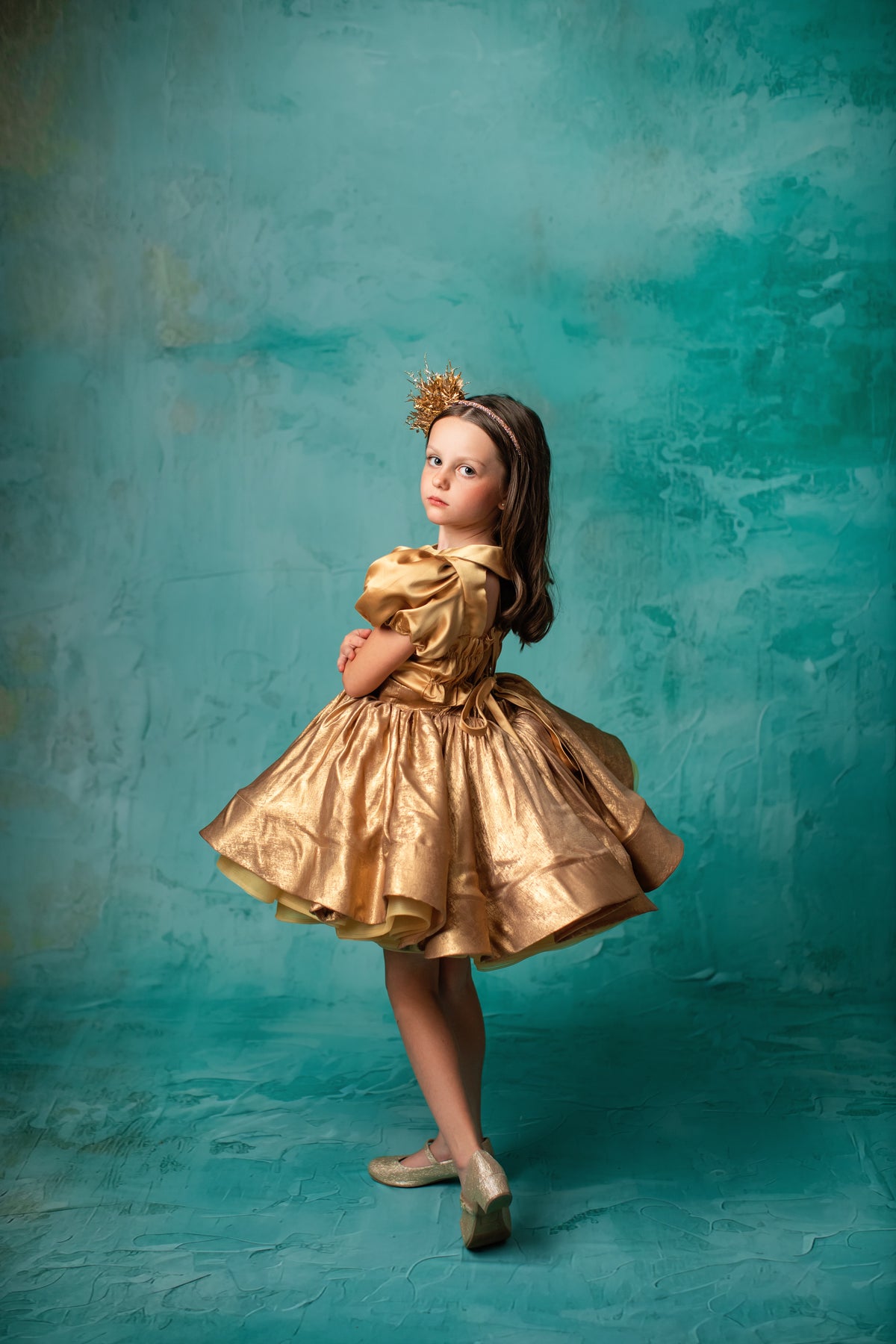 "Child model twirling in a radiant gold dress with a shiny, textured finish."