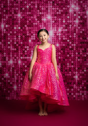 Young girl in a pink dress standing against a pink sequin backdrop