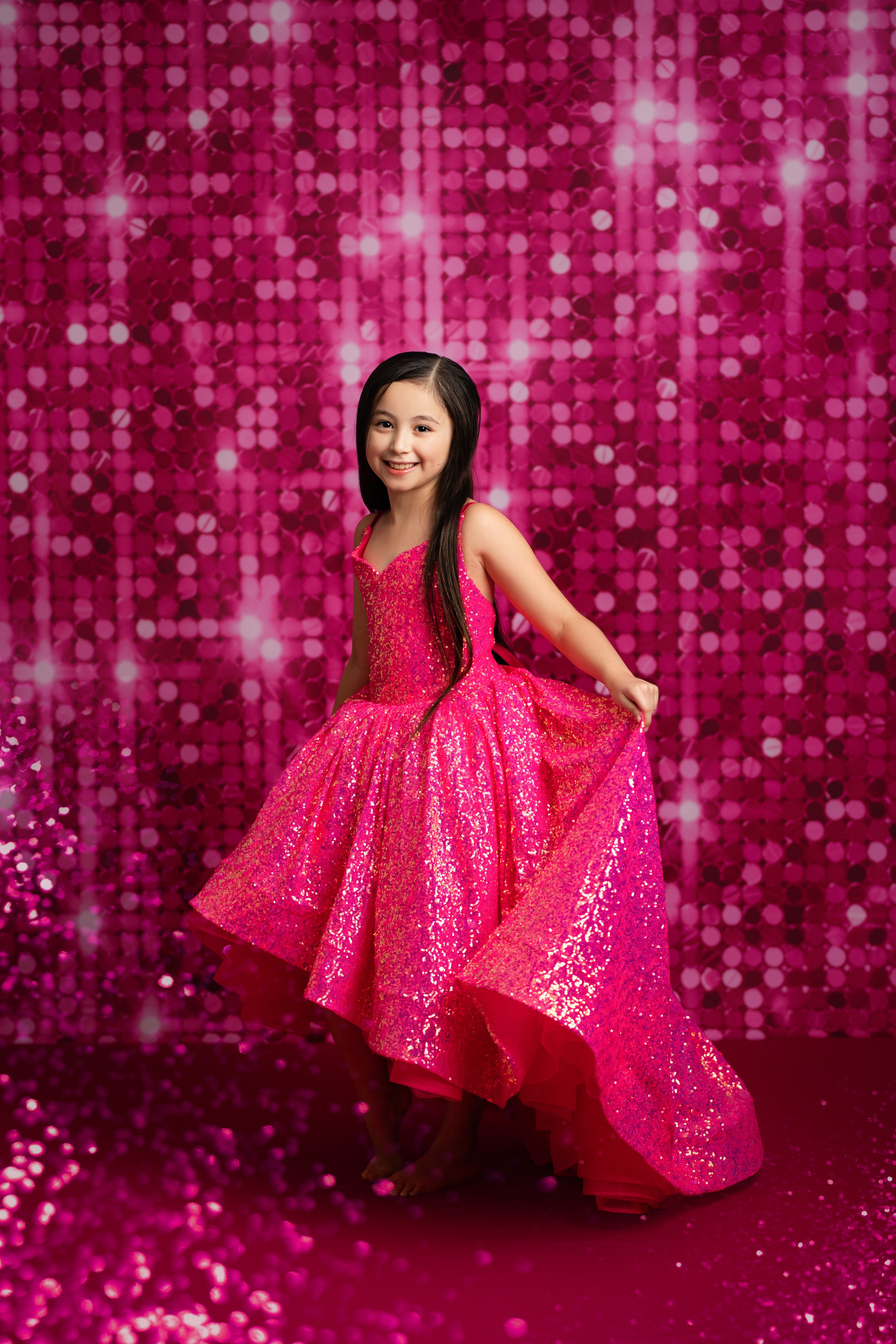 Young girl in a pink sequin dress posing against a pink sequin backdrop