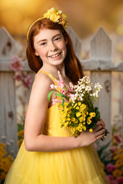 Golden glow – The warmth of the golden hour enhances the beauty of a girl in a tulle gown, standing softly against a floral-accented fence.

