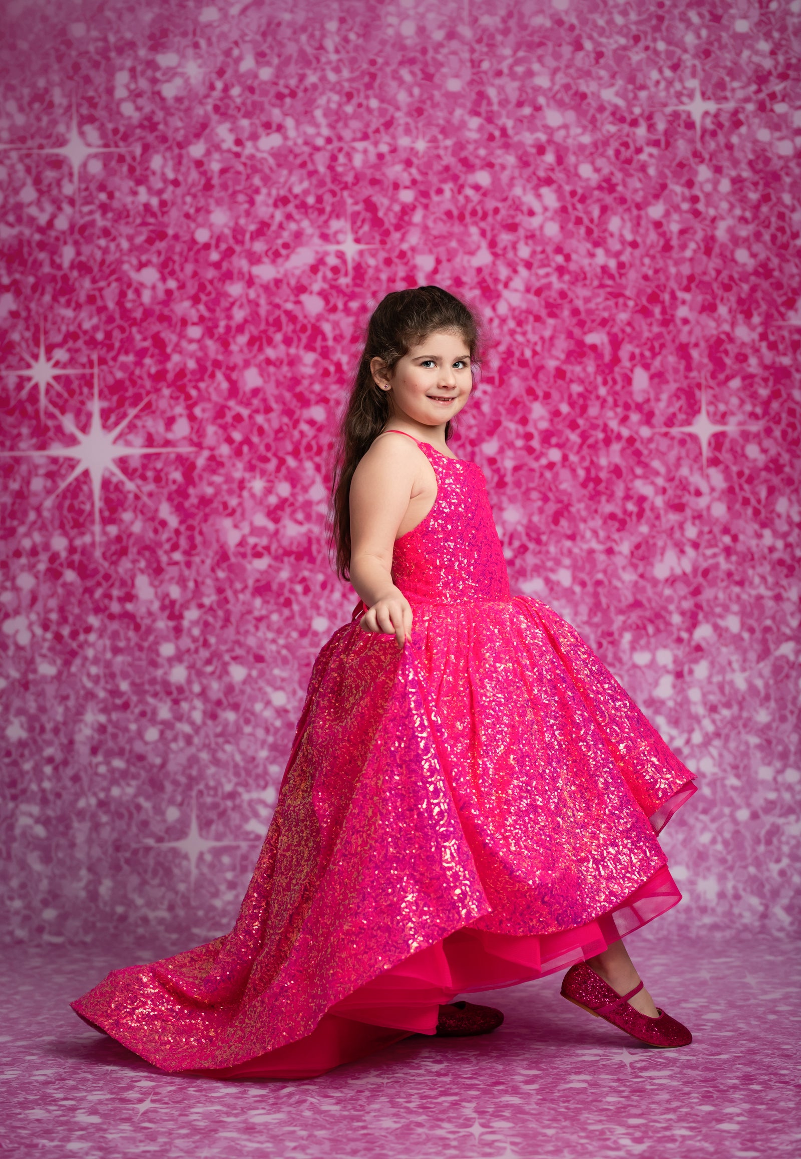 Young girl in a bright pink dress against a pink starry background