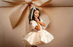 Young girl in a white dress standing in front of a large beige bow