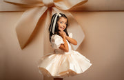 Young girl in a white dress standing in front of a large beige bow