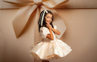 Young girl in a white dress standing in front of a large beige bow