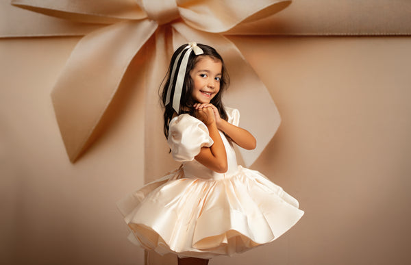 Young girl in a white dress standing in front of a large beige bow