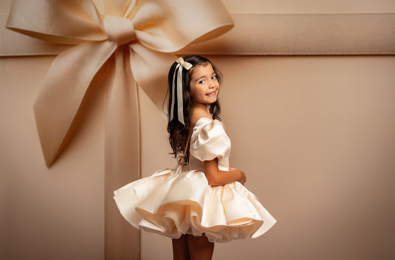 Young girl in a white dress standing next to a large gift box with a bow on a beige background
