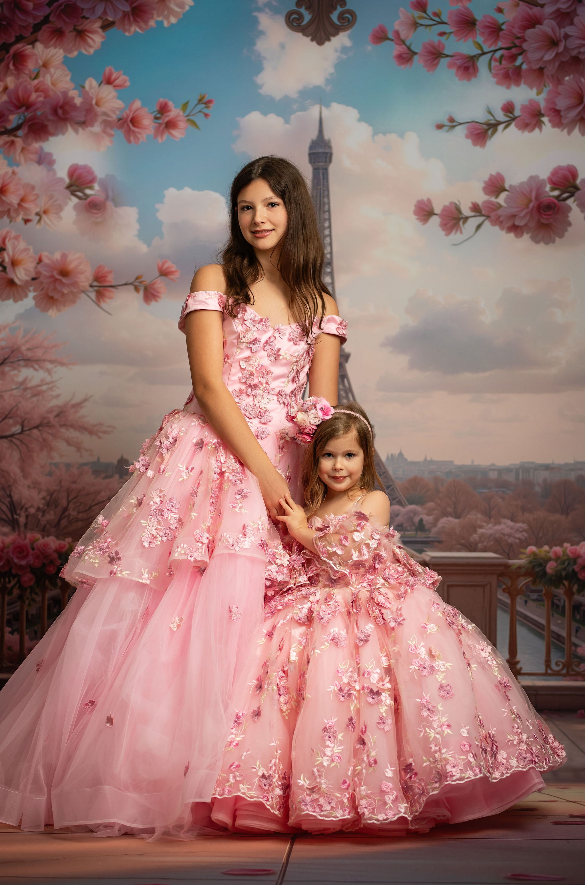 Two women in pink dresses standing in front of the Eiffel Tower with cherry blossom trees.