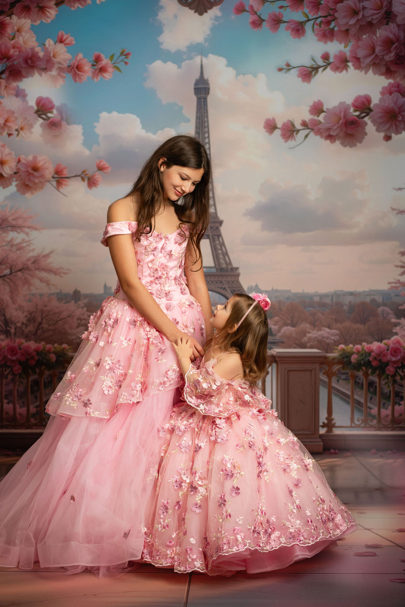 Two women in pink dresses standing in front of the Eiffel Tower with cherry blossom trees.