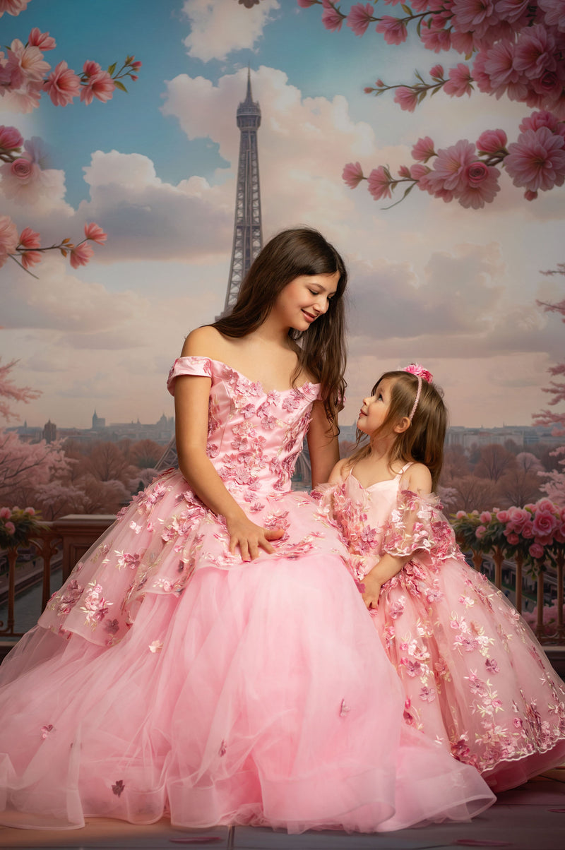 Two girls in pink dresses with floral details sitting in front of the Eiffel Tower.