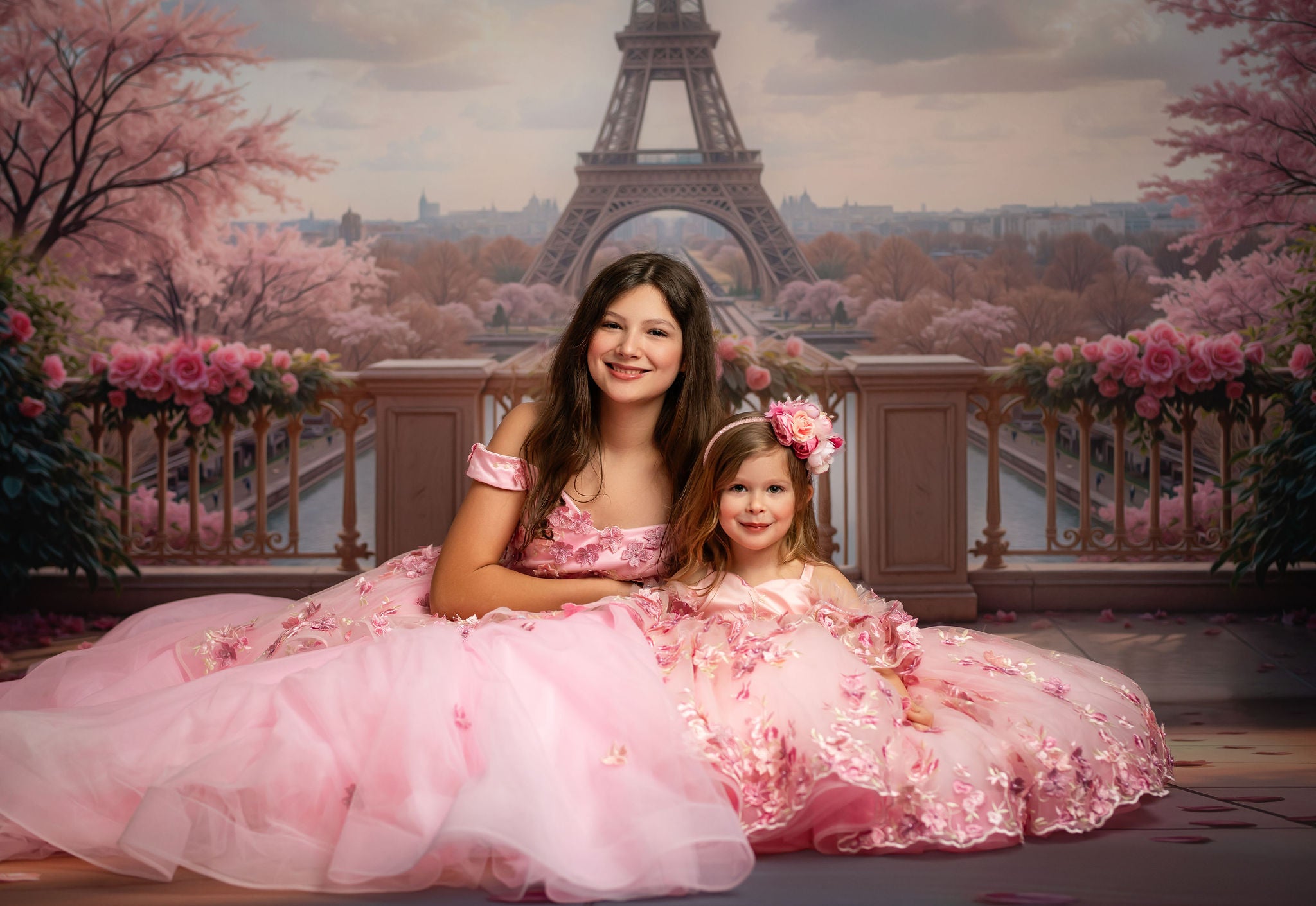 Two girls in pink dresses posing in front of a scenic backdrop with cherry blossoms and the Eiffel Tower.