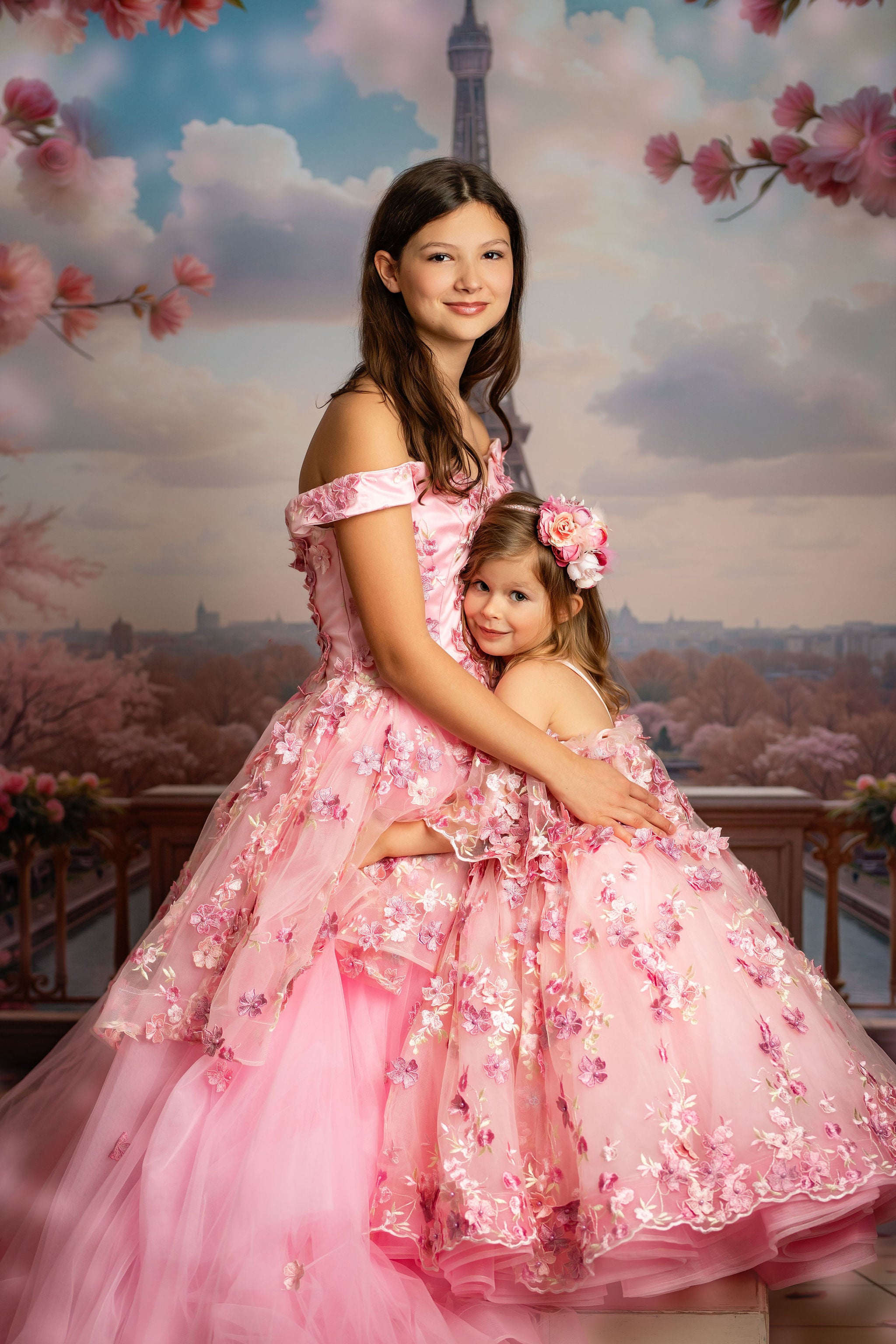 Two women in pink dresses with floral designs against a scenic backdrop with cherry blossoms.
