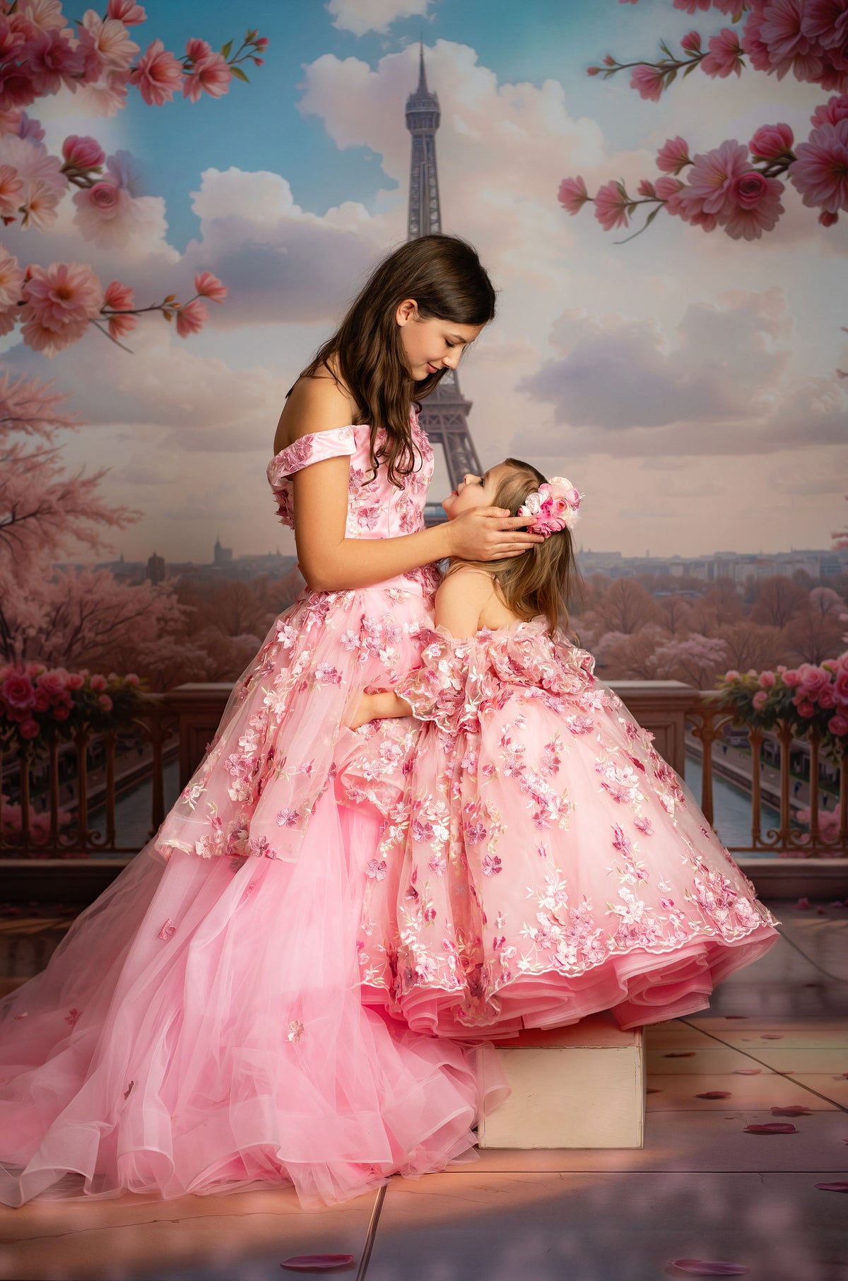 Two women in pink dresses standing in front of the Eiffel Tower with cherry blossoms.
