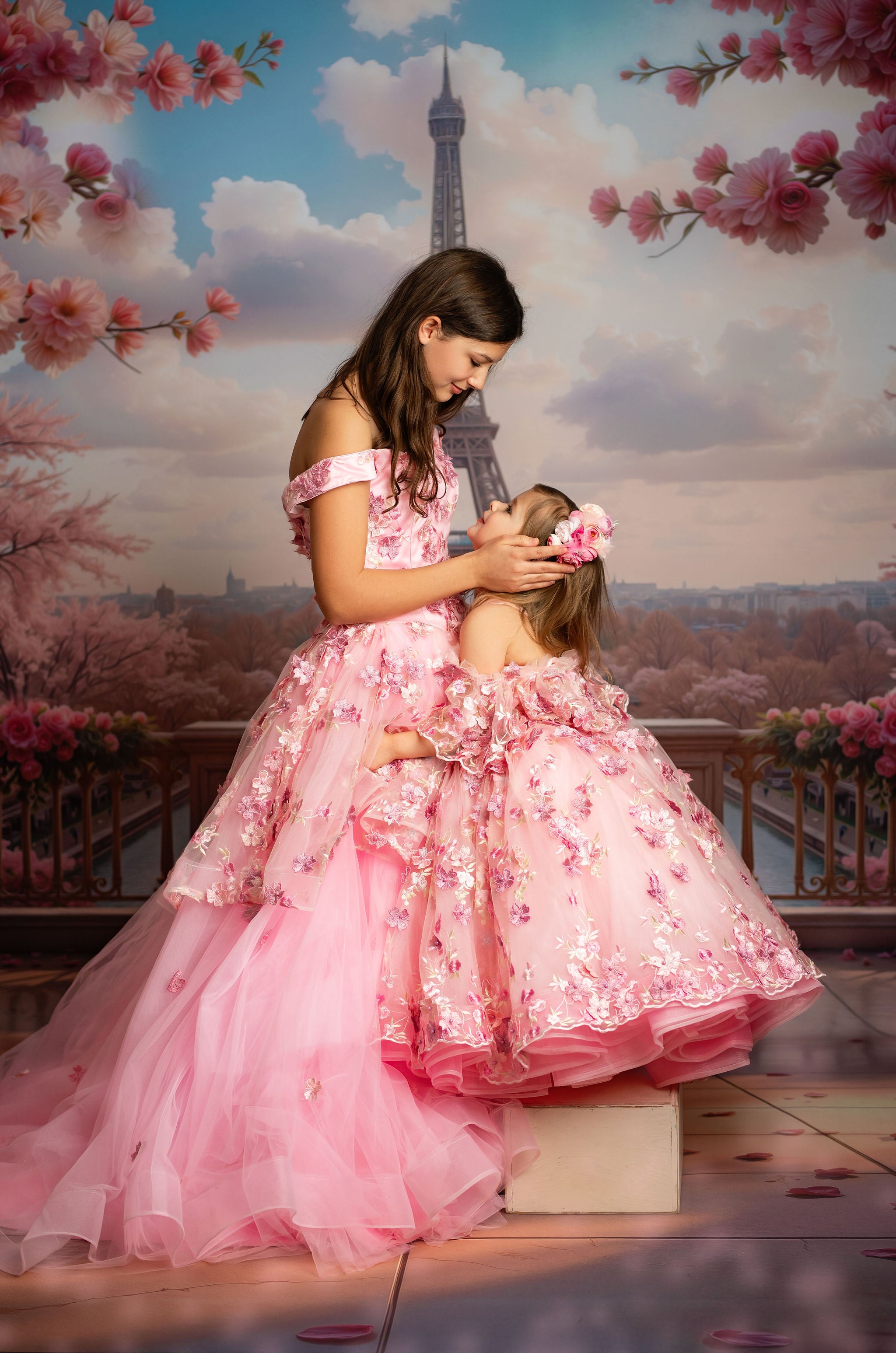 Two women in pink dresses standing in front of the Eiffel Tower with cherry blossoms.