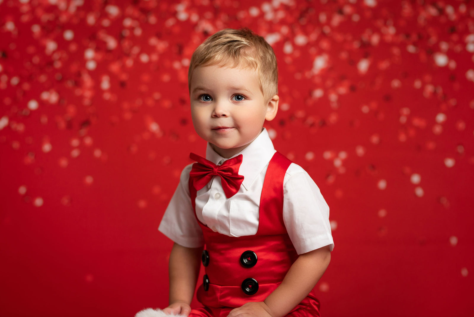 Child in a red outfit with suspenders and bow tie against a red background