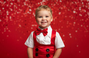 Child wearing a red vest and bow tie against a red background with white polka dots