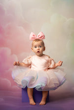 Baby in a pink dress with a large bow on a colorful background