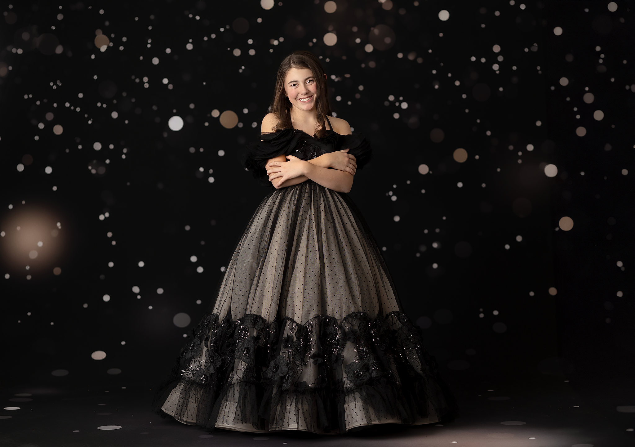 Model twirling in a voluminous black gown with a flowing layered skirt and sparkling sequin embellishments.