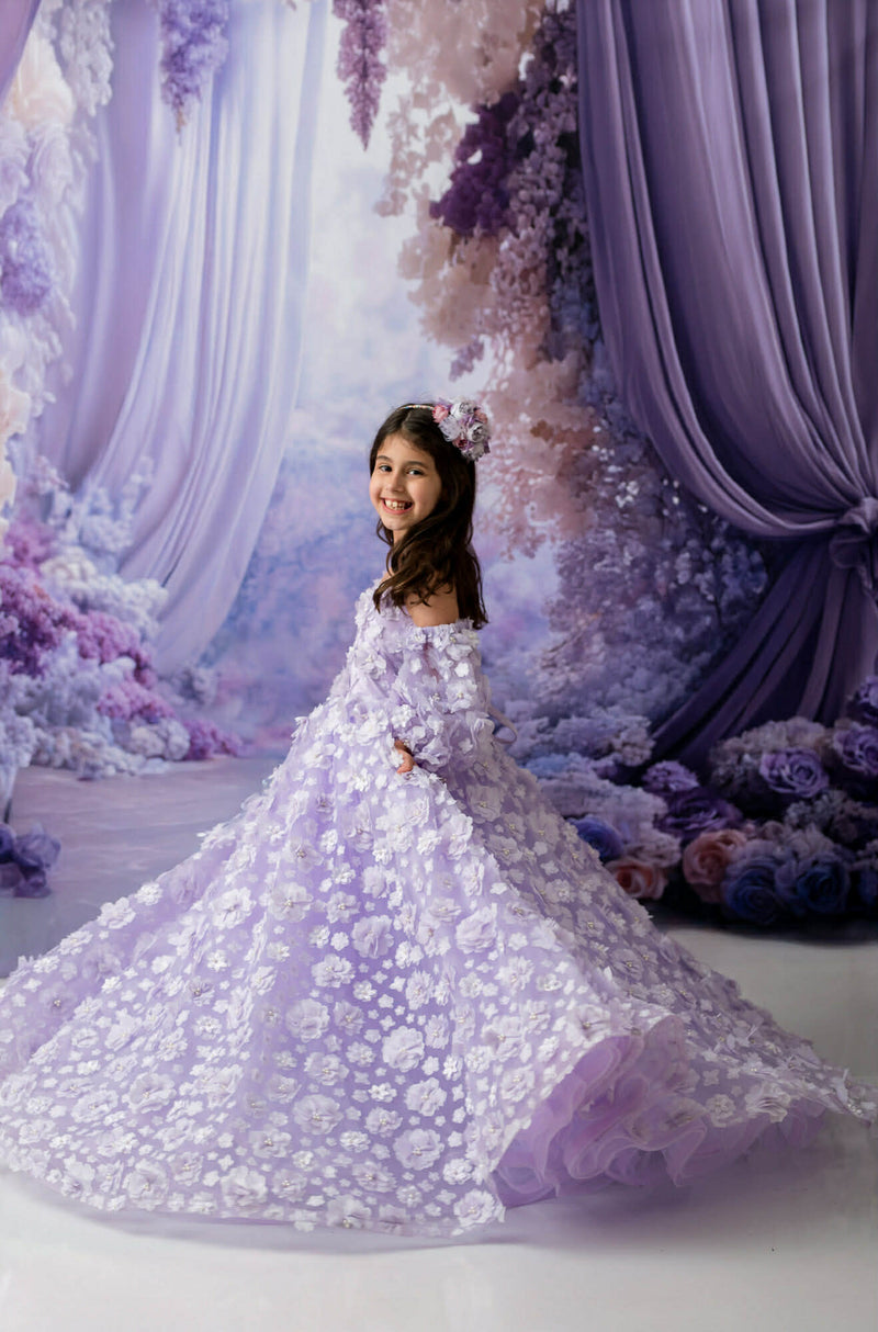 Young girl in a white floral dress standing in front of a decorative floral and curtain backdrop.