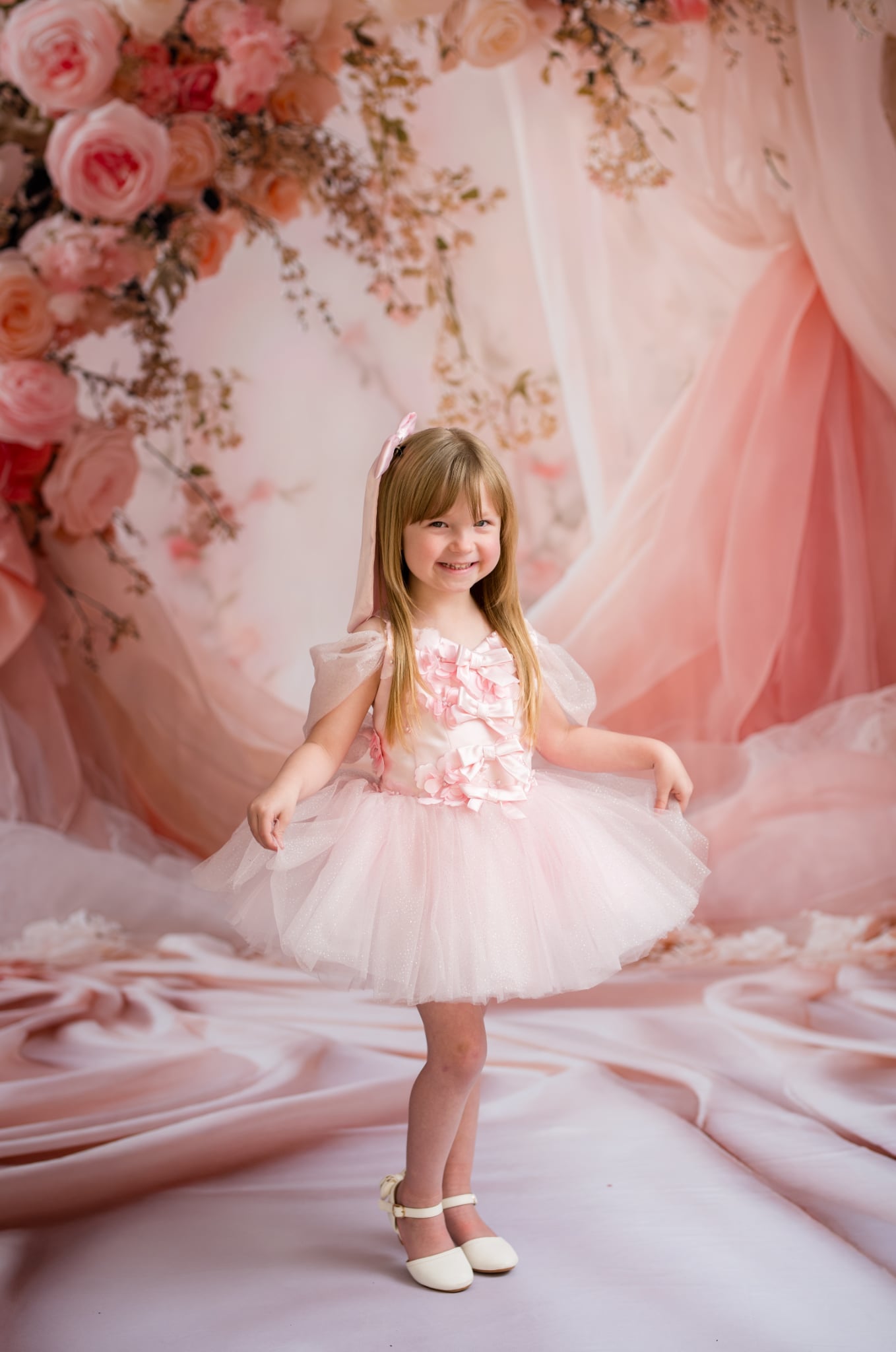 Young girl in a floral dress standing in front of a pink floral backdrop
