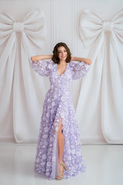 Woman in a purple floral dress posing against a white curtain with large bows.