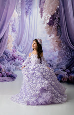 Woman in a lavender floral dress standing in a fantasy-like setting with floral decorations and soft lighting.