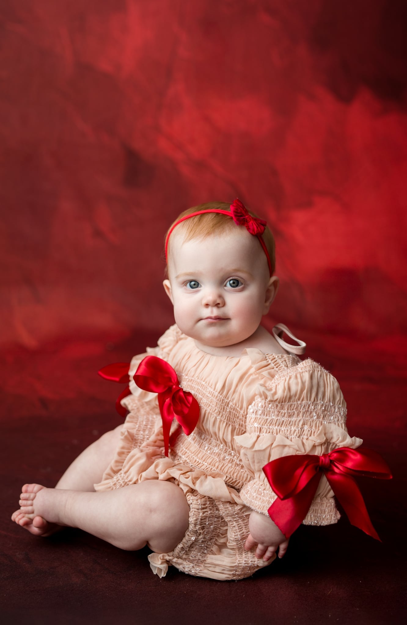 Baby in a beige dress with red bows against a red background