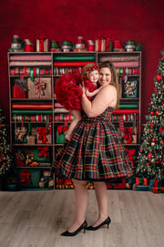 Holiday family photography with mom and children in coordinating red, green, and plaid outfits, Christmas-themed background.