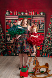 Festive mother-daughter Christmas portrait with plaid dress, green and red holiday outfits, and holiday backdrop.