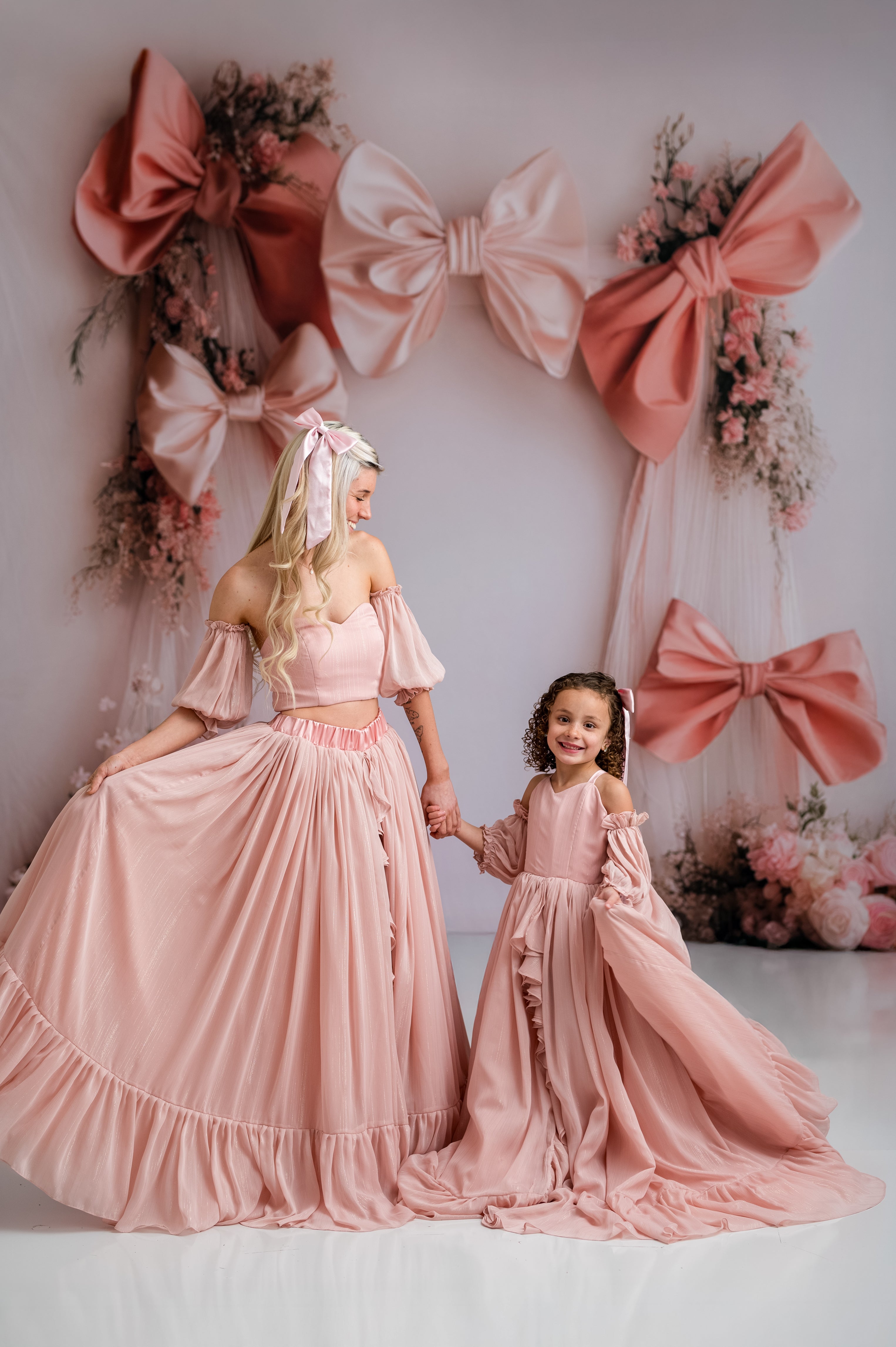 Two women in matching pink dresses standing in front of decorative bows and flowers.