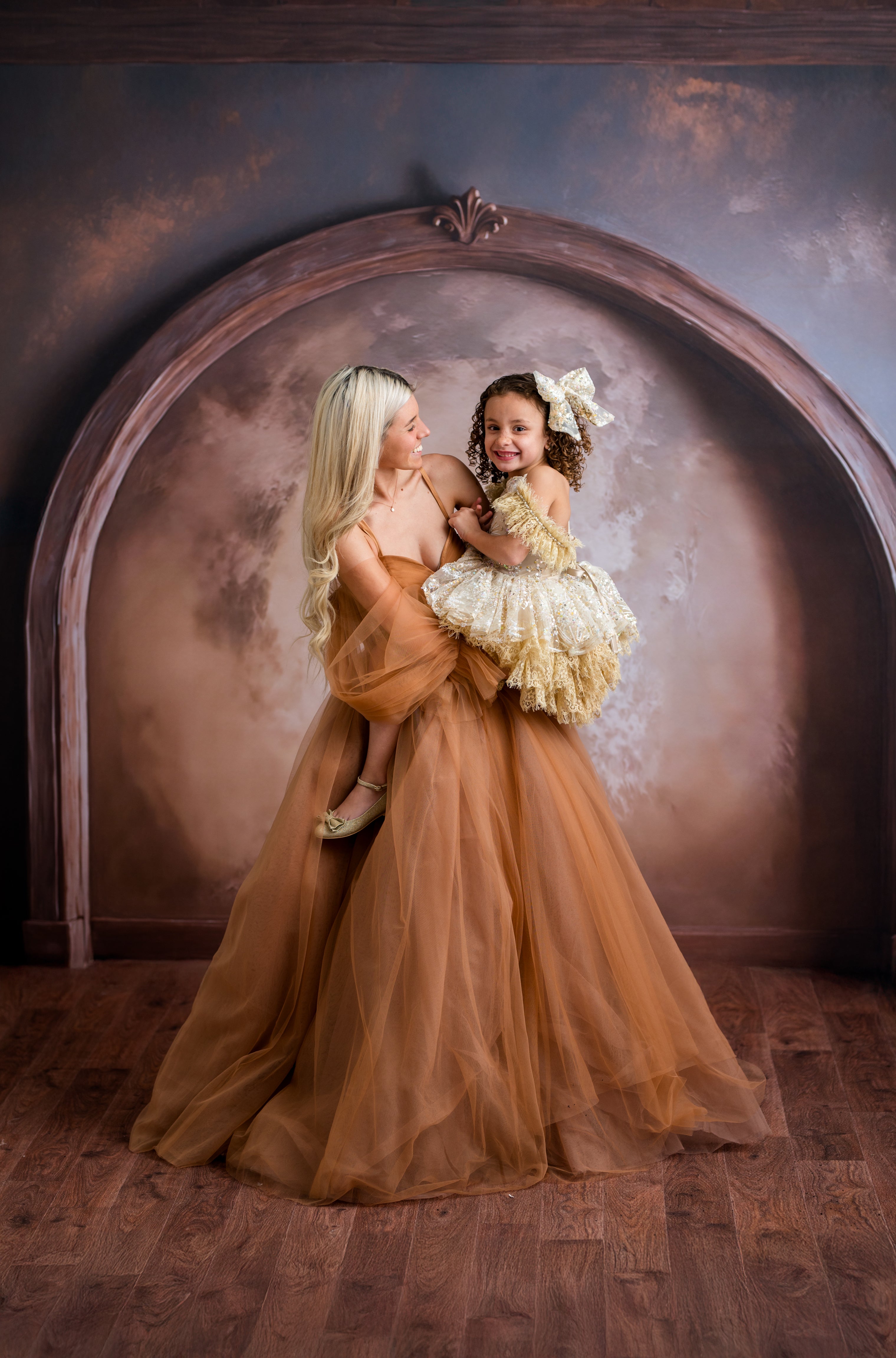 Woman in a long, flowing dress holding a child in a decorative setting with an archway.