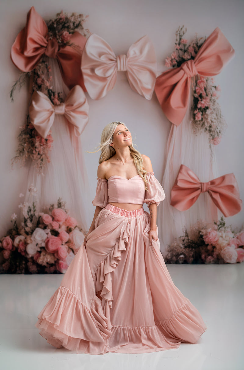Woman in a pink dress standing in front of decorative bows and flowers.