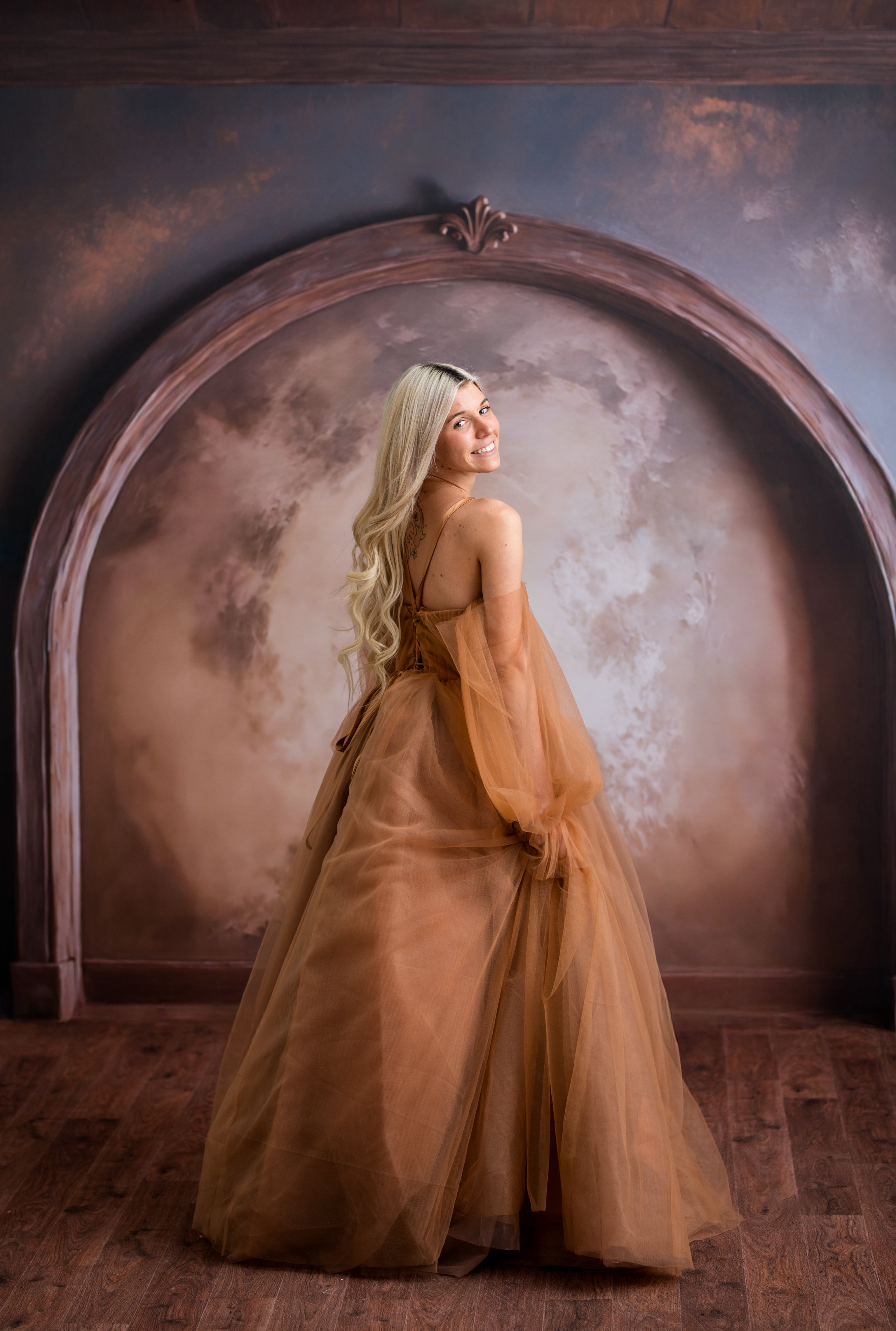 Woman in a long, flowing dress standing in front of an archway with a textured wall.