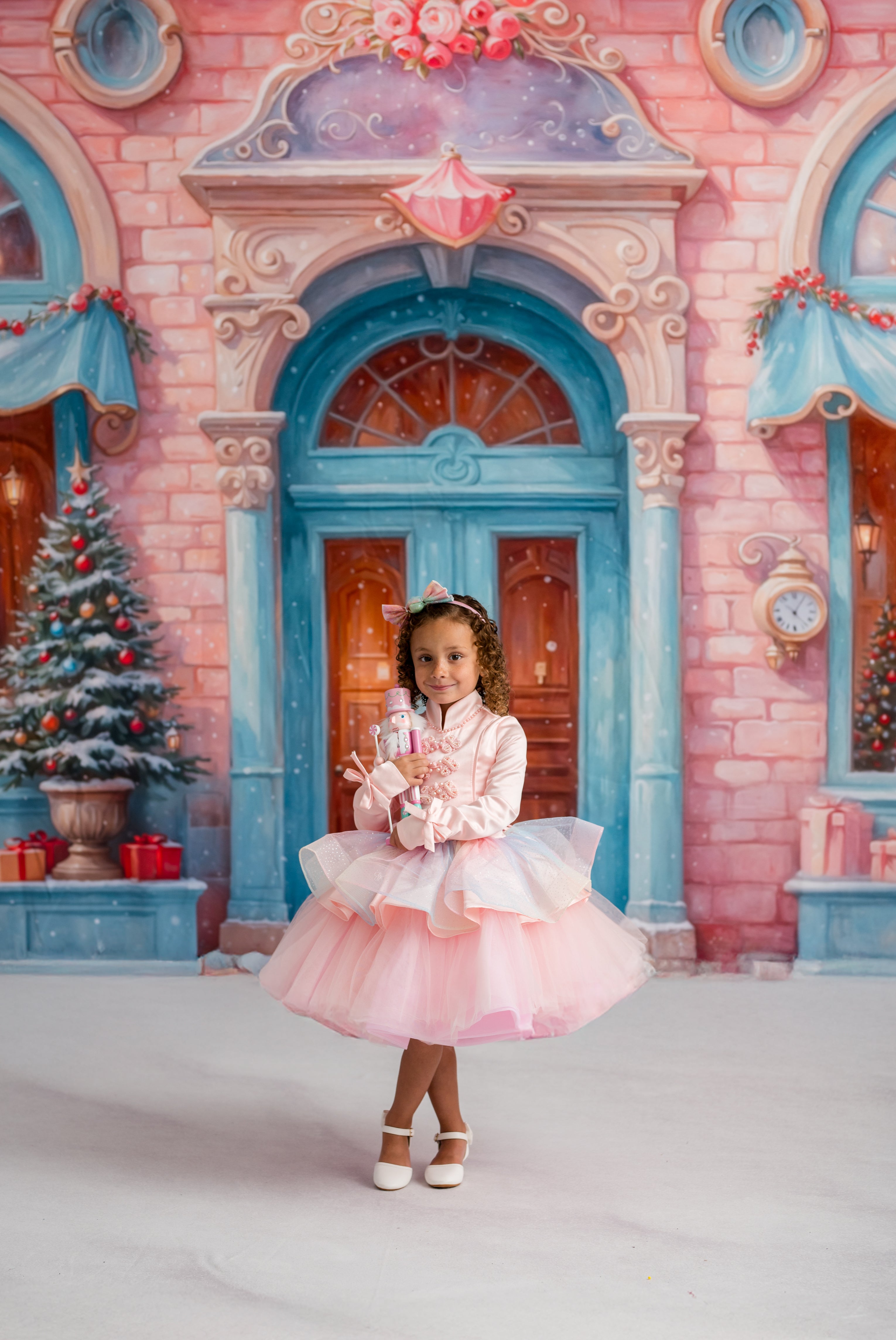 Young girl in a pink dress standing in front of a fairy-tale castle with Christmas decorations.