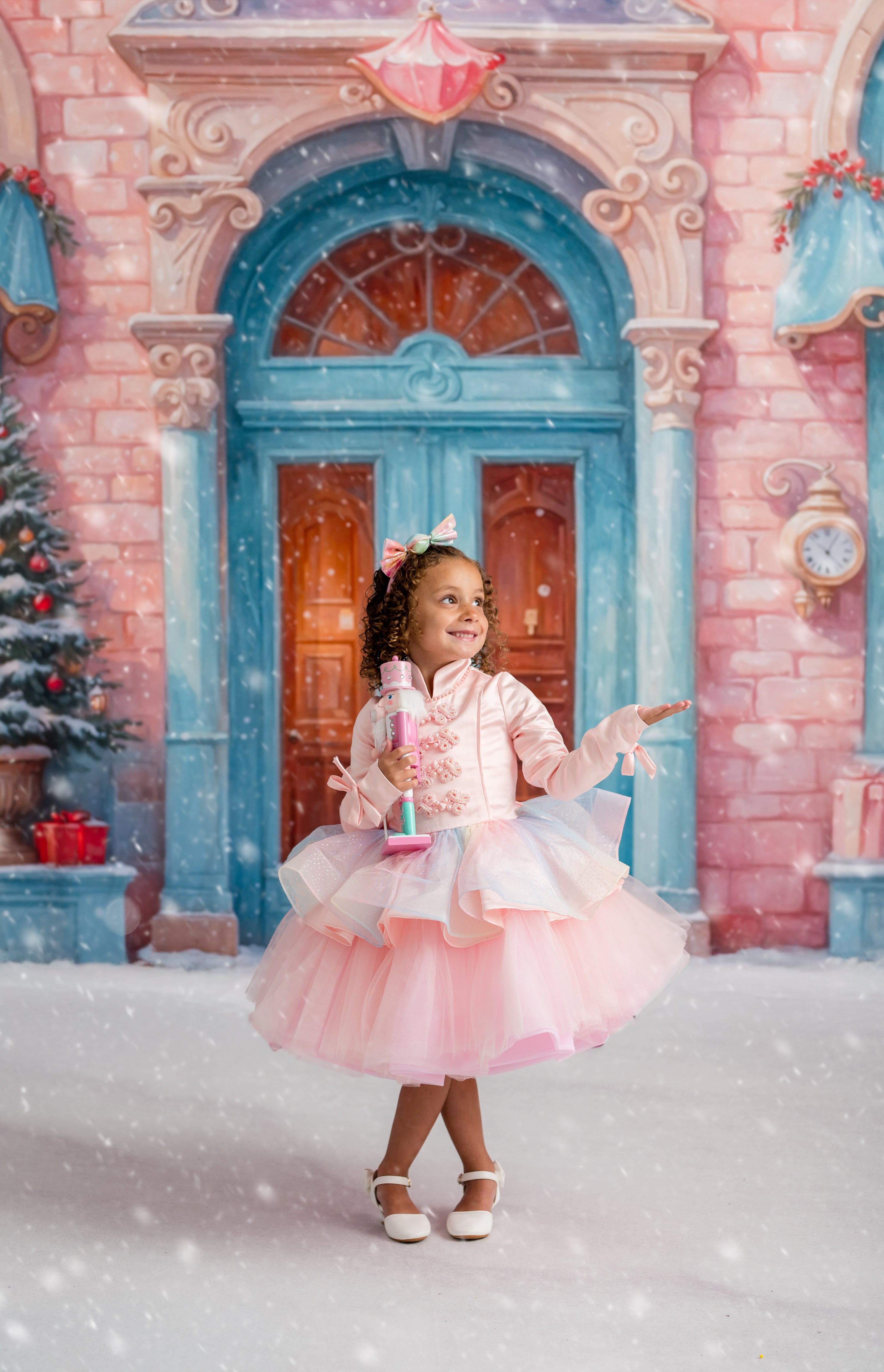 Young girl in a pink dress standing in front of a festive door with Christmas decorations.