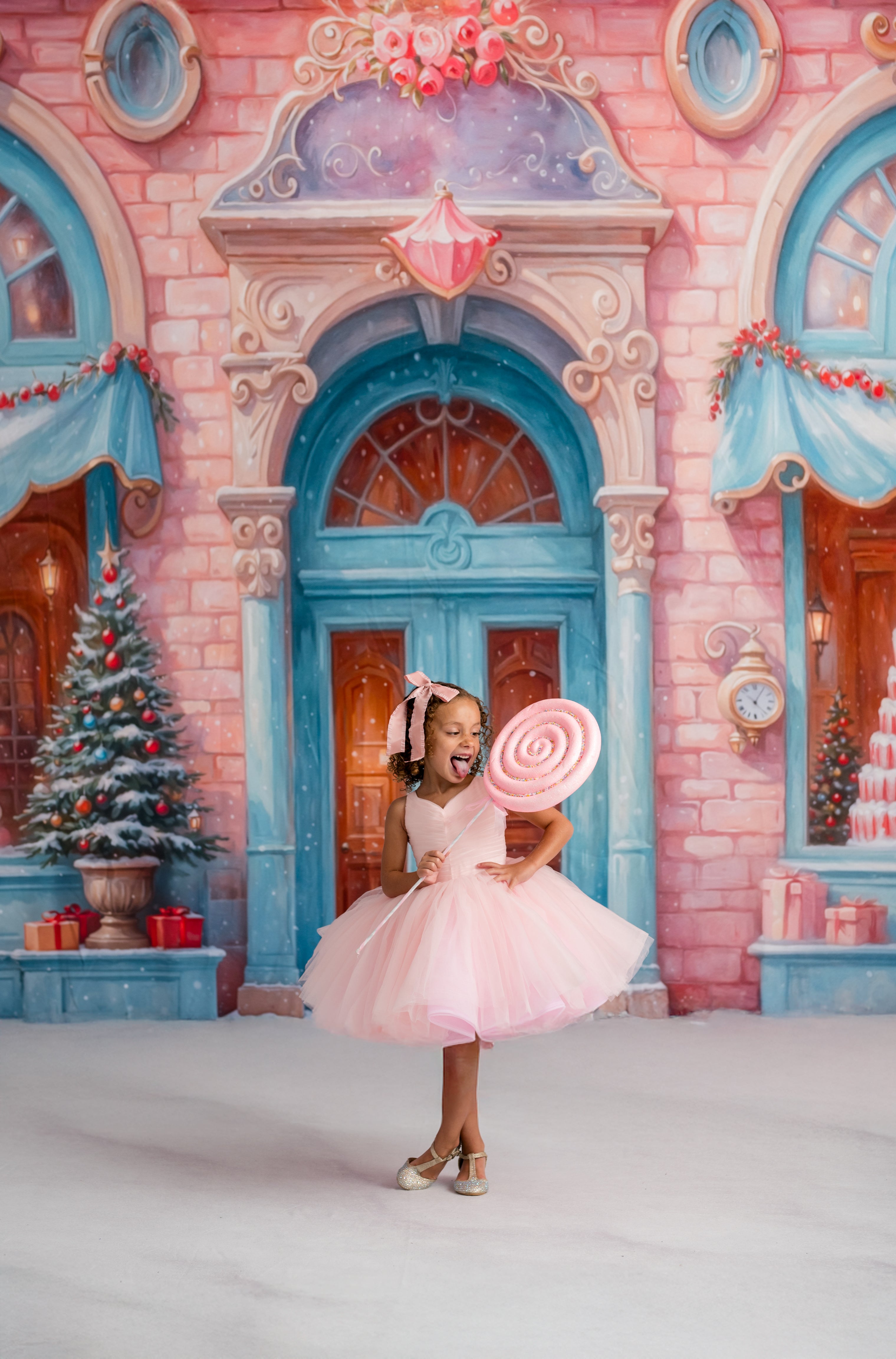 Young girl in a pink dress holding a candy in front of a colorful, fantasy-style building.