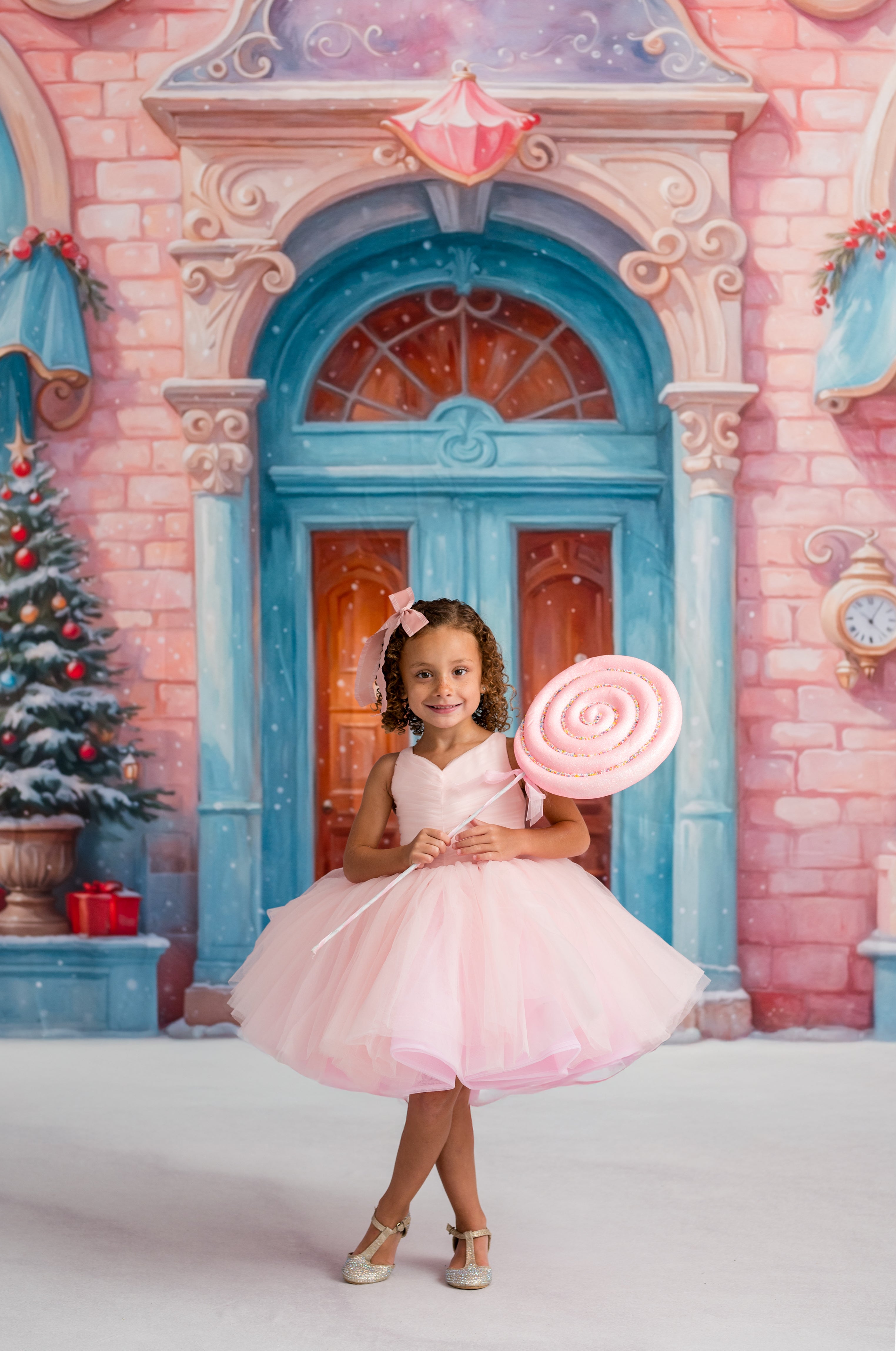 Young girl in a pink dress holding a candy cane in front of a fairy-tale castle backdrop.