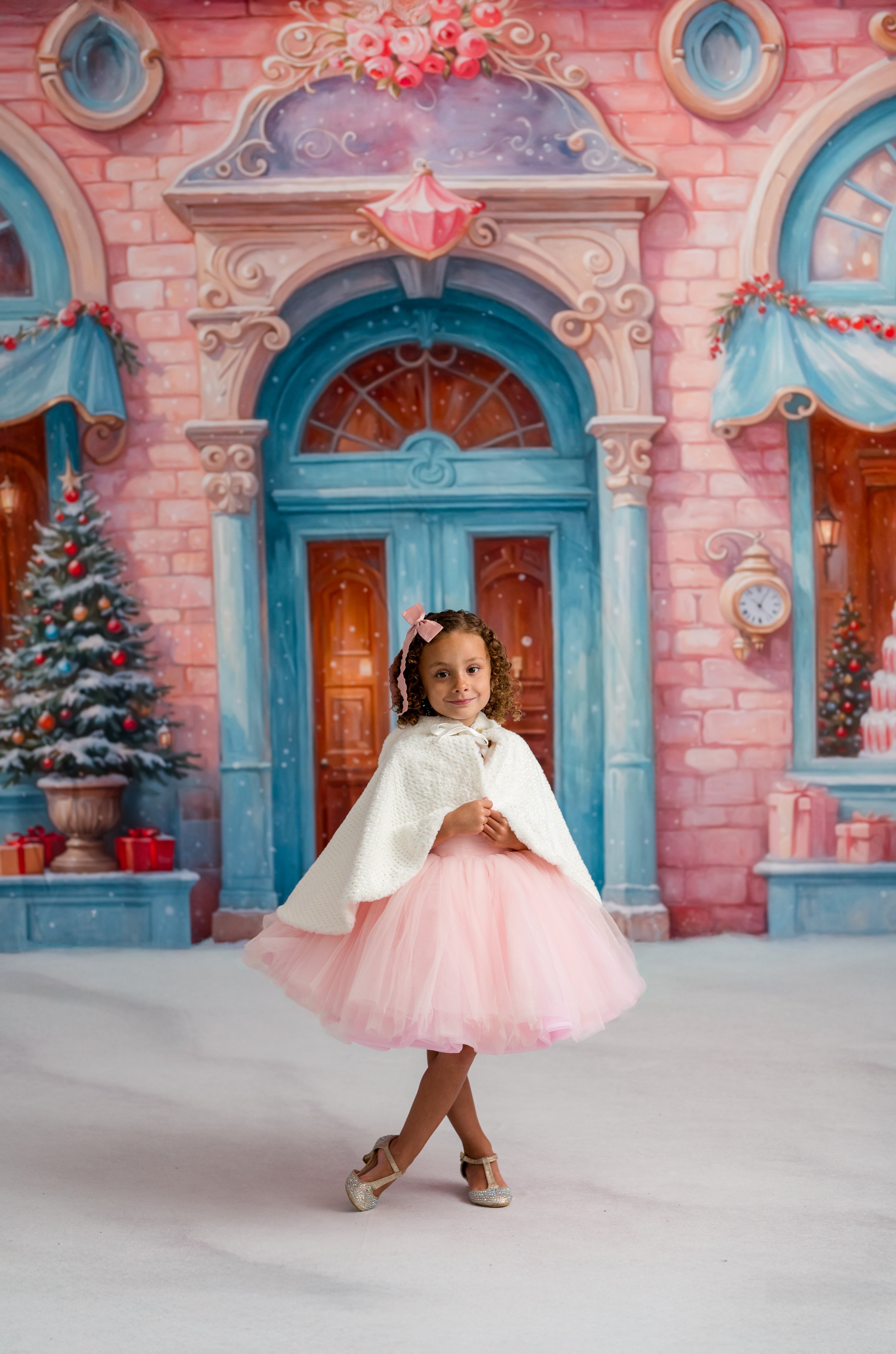 Young girl in a pink dress and white cape standing in front of a decorative castle backdrop.