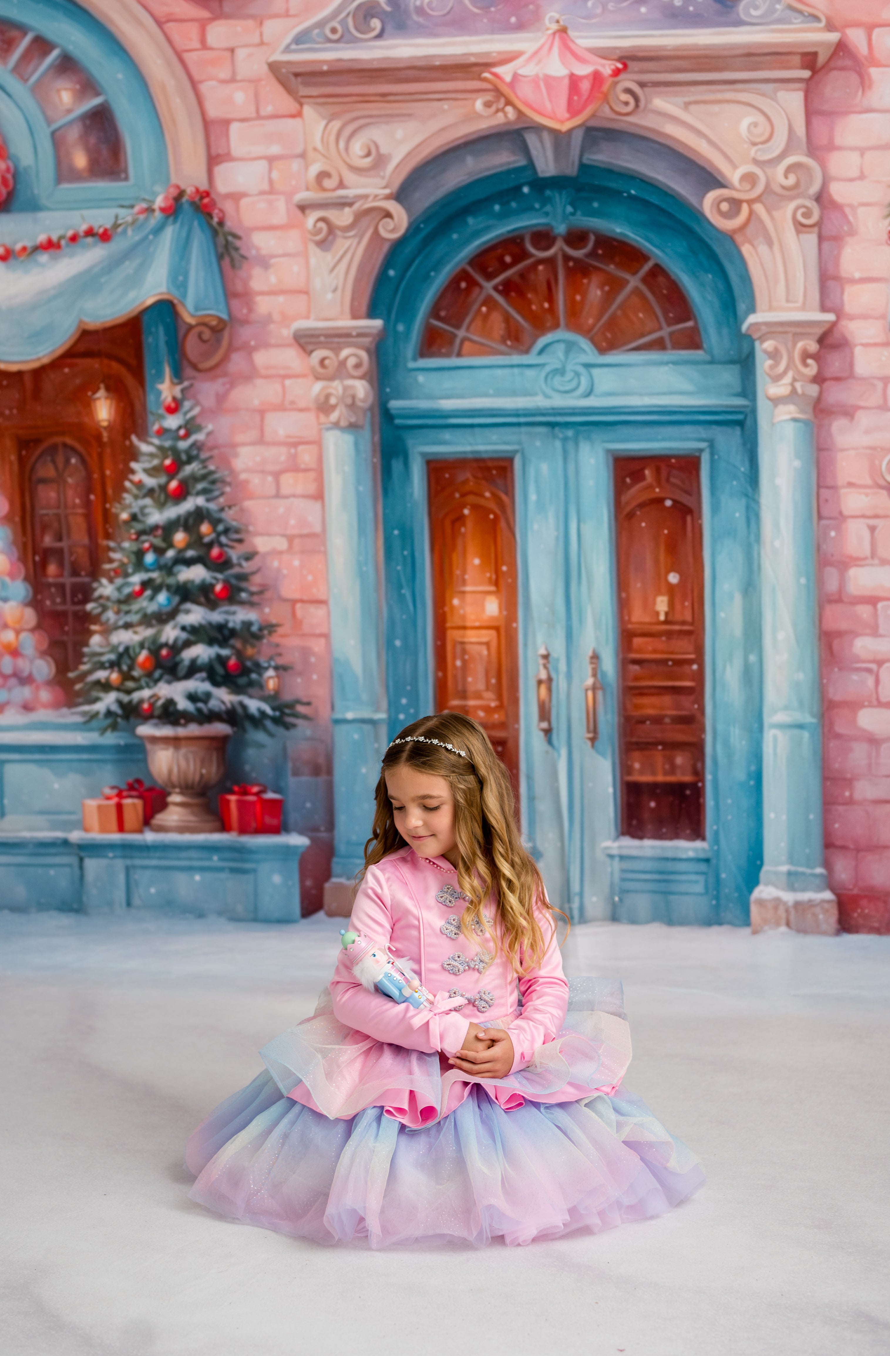 Young girl in a pink dress sitting in front of a fairy tale castle with a Christmas tree.
