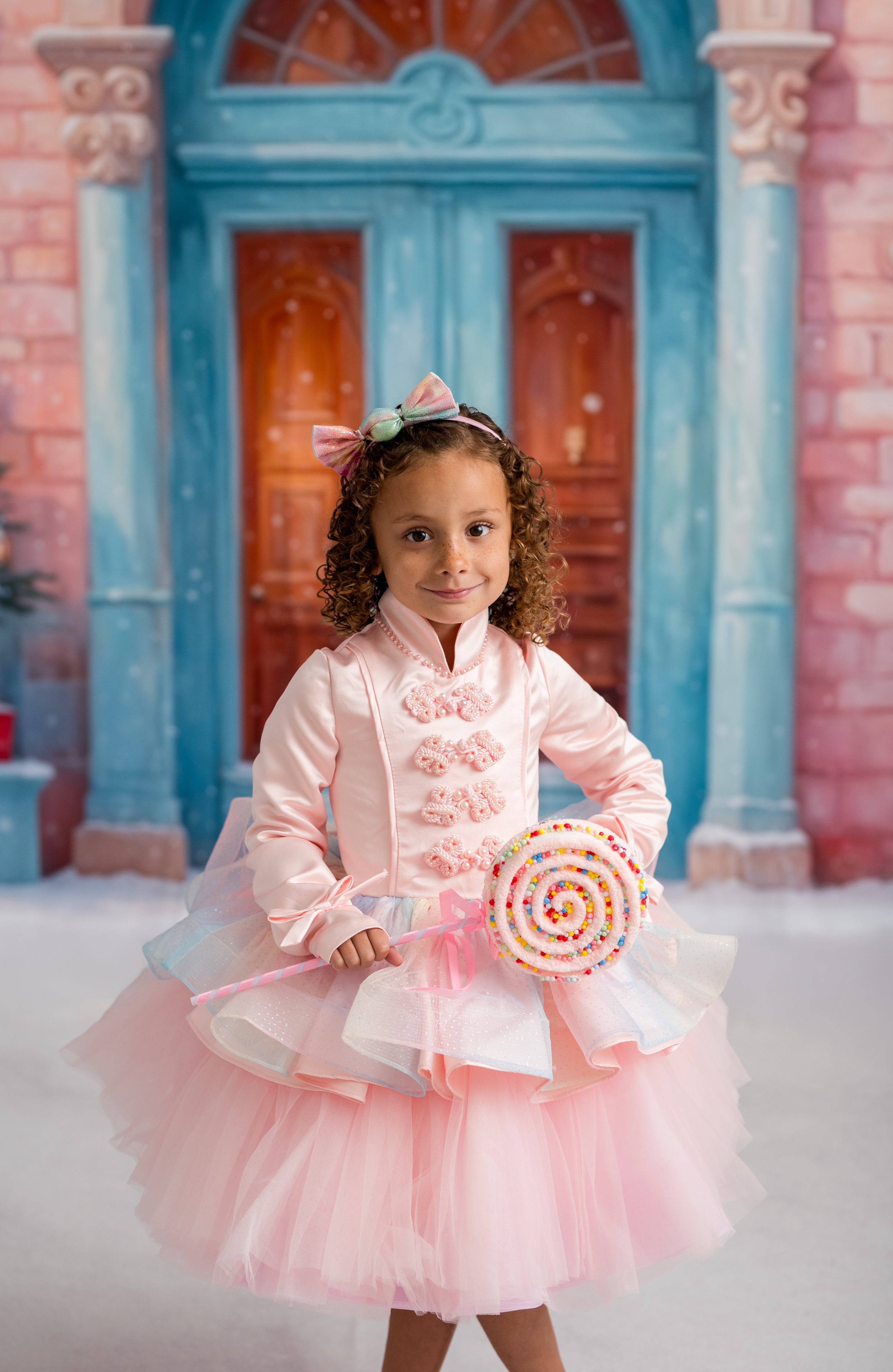 Young girl in a pink dress with floral details standing in front of a colorful building.