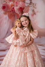 Young girl in a pink dress holding a doll against a floral backdrop