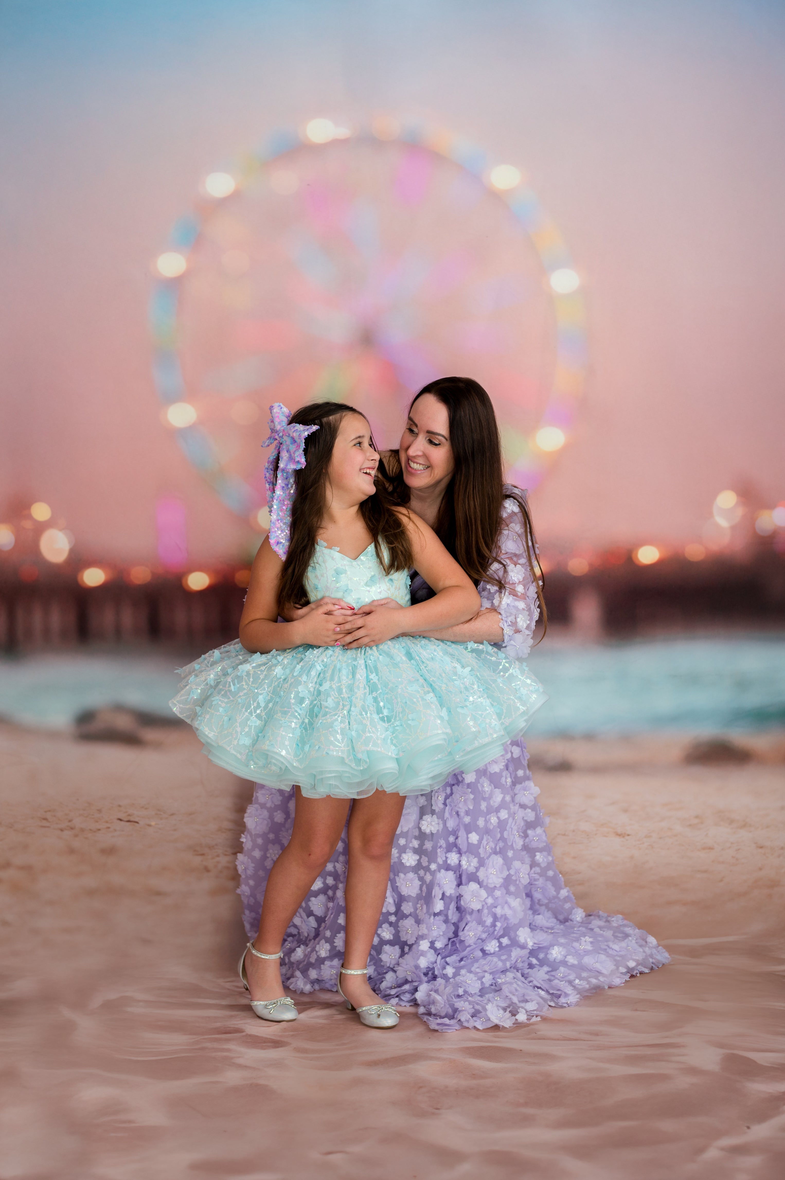 Two women in matching dresses standing on a beach with a Ferris wheel in the background.