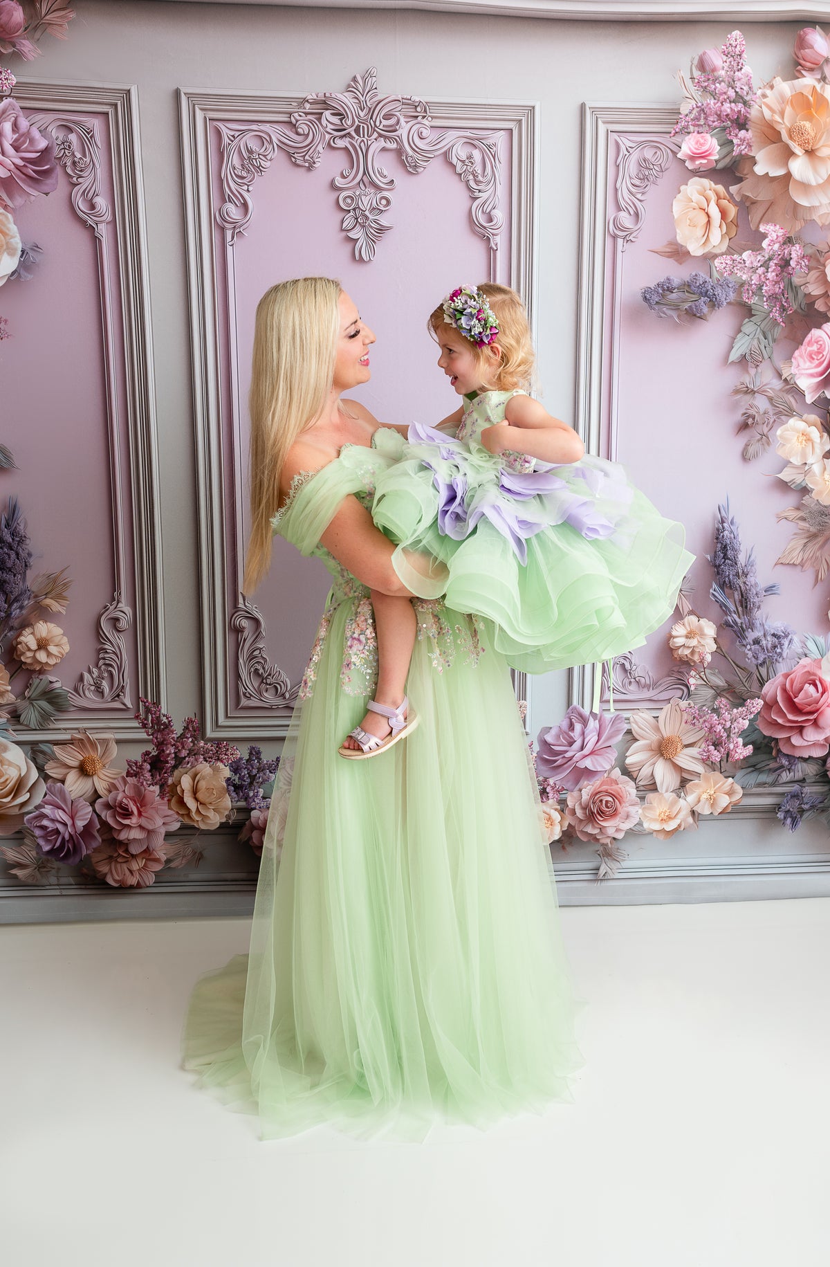 Mother holding her daughter in coordinating green Bentley and Lace couture gowns during a Mommy and Me portrait session