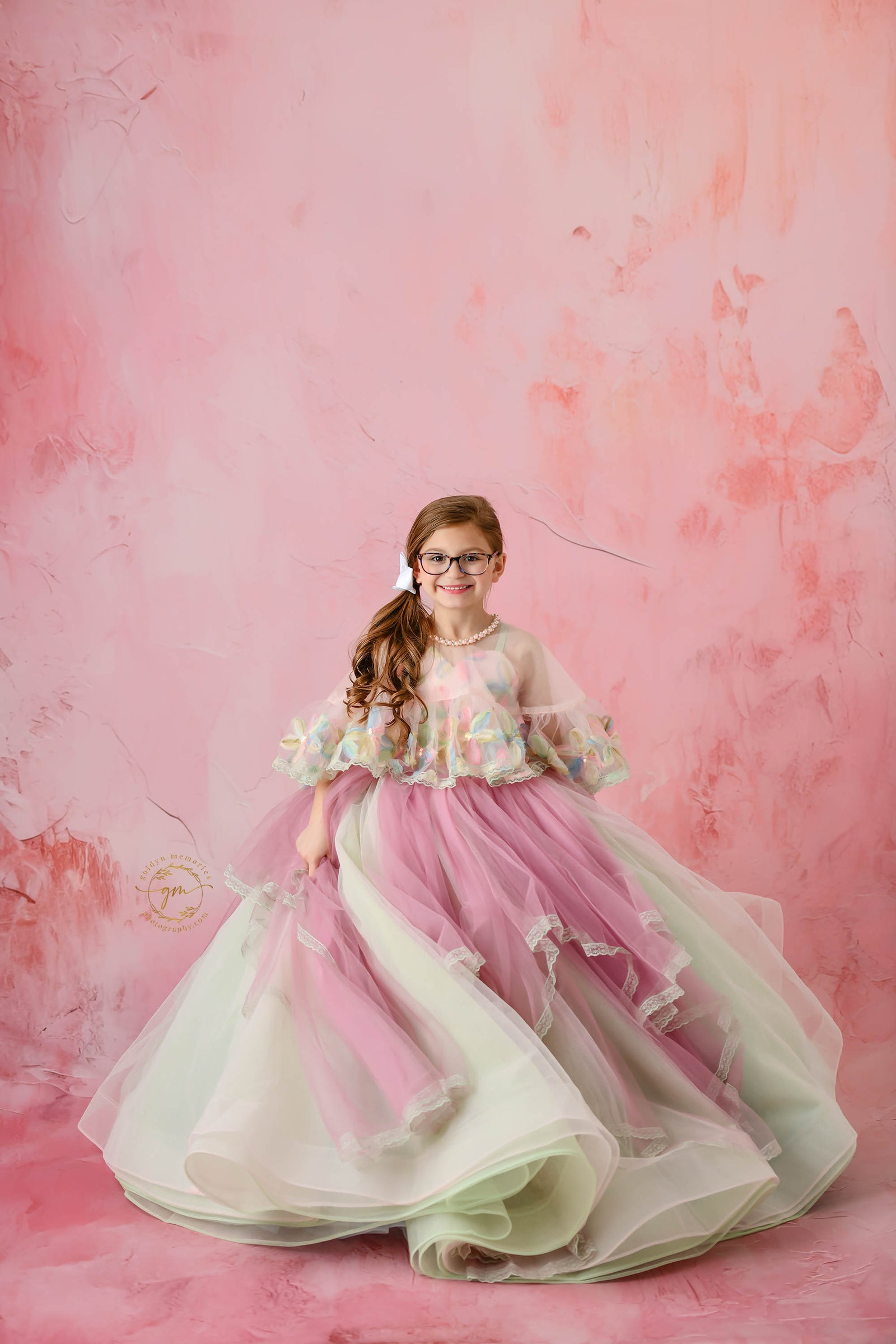 Elegant floral gown drapes around a young girl, showcasing its intricate and colorful design.
