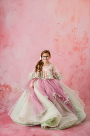 Elegant floral gown drapes around a young girl, showcasing its intricate and colorful design.
