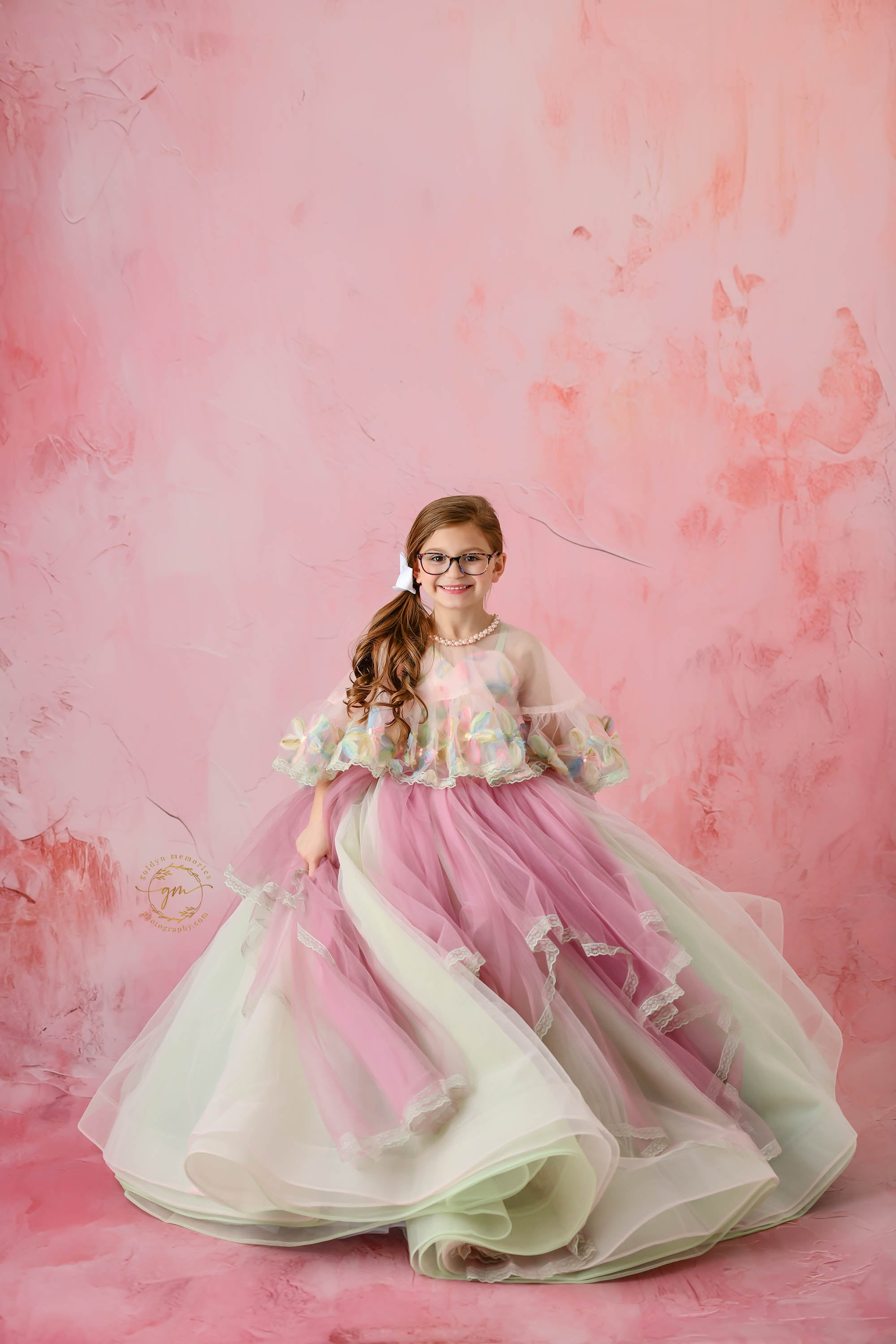 Elegant floral gown drapes around a young girl, showcasing its intricate and colorful design.
