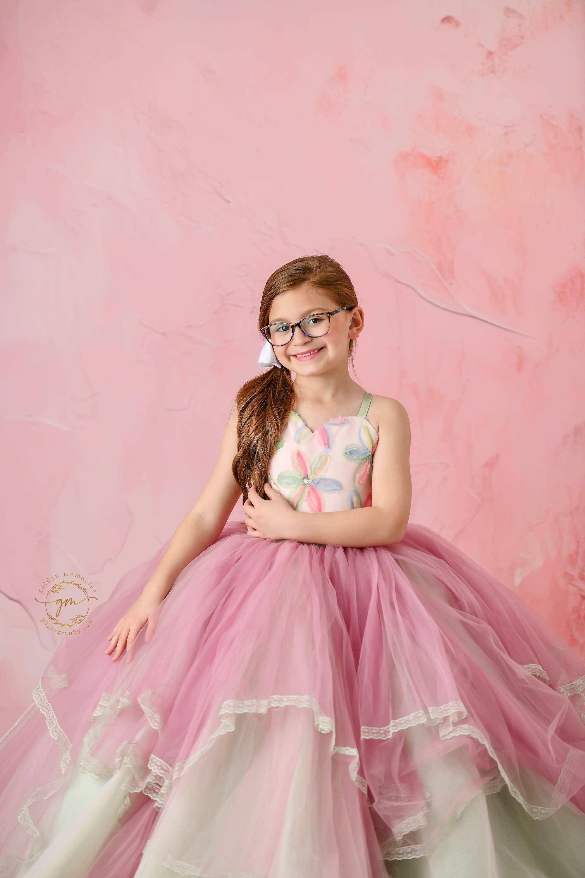 A joyful young girl posing in a beautifully patterned floral gown with flowing layers.
