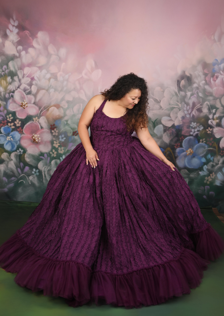 Woman in a purple gown standing against a floral mural.
